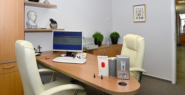 Modernes Arztpraxis-Büro mit Schreibtisch, Computer, medizinischem Equipment und Stühlen.